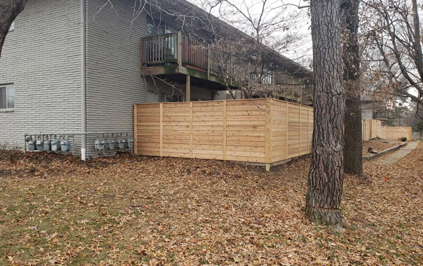 A wooden fence is in front of a house with a deck.