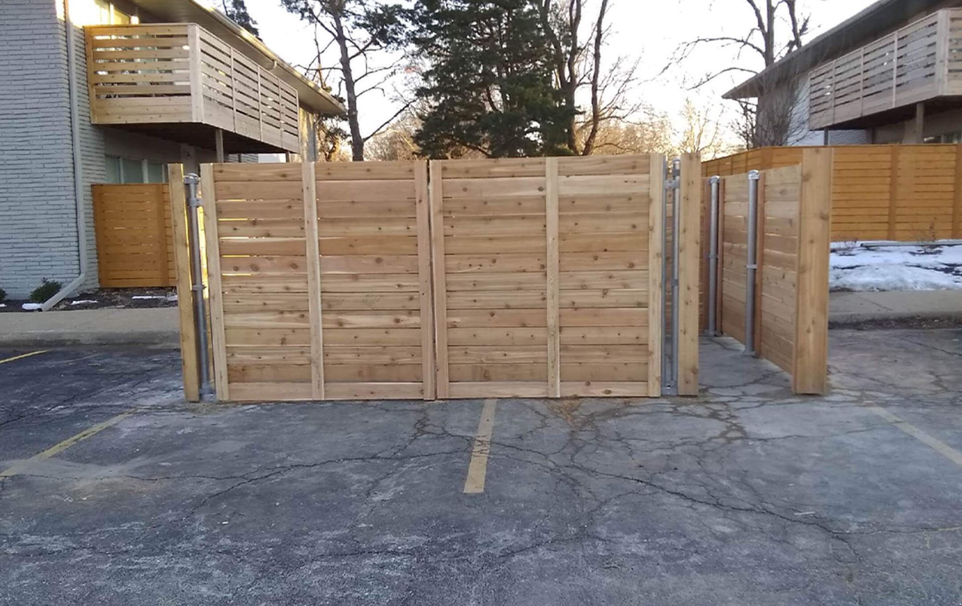 A wooden fence is in a parking lot in front of a building