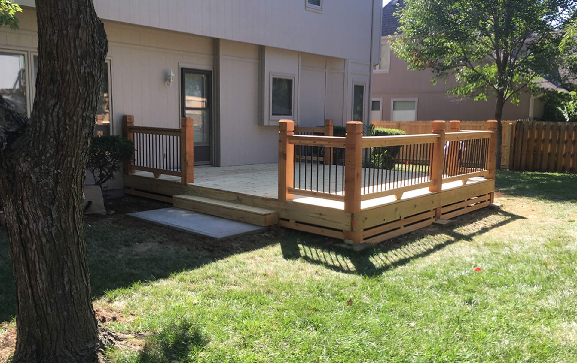 A wooden deck with a railing in the backyard of a house.