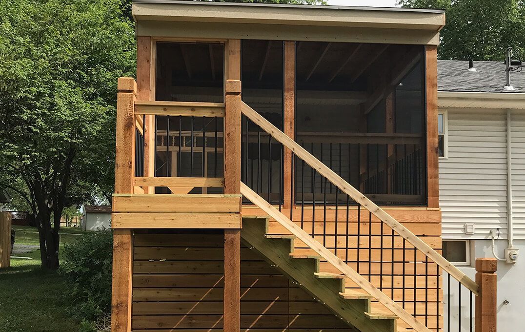 A wooden deck with stairs leading up to it and a screened in porch.