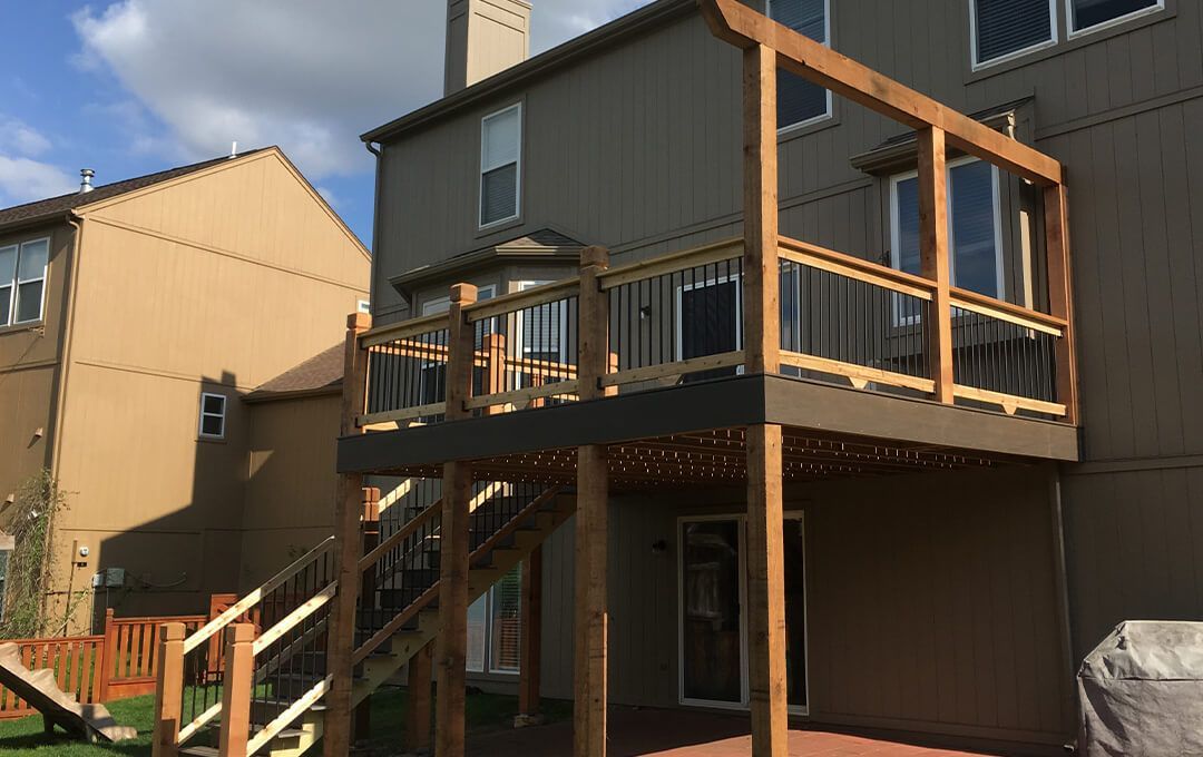 A wooden deck with stairs leading up to it is in the backyard of a house.