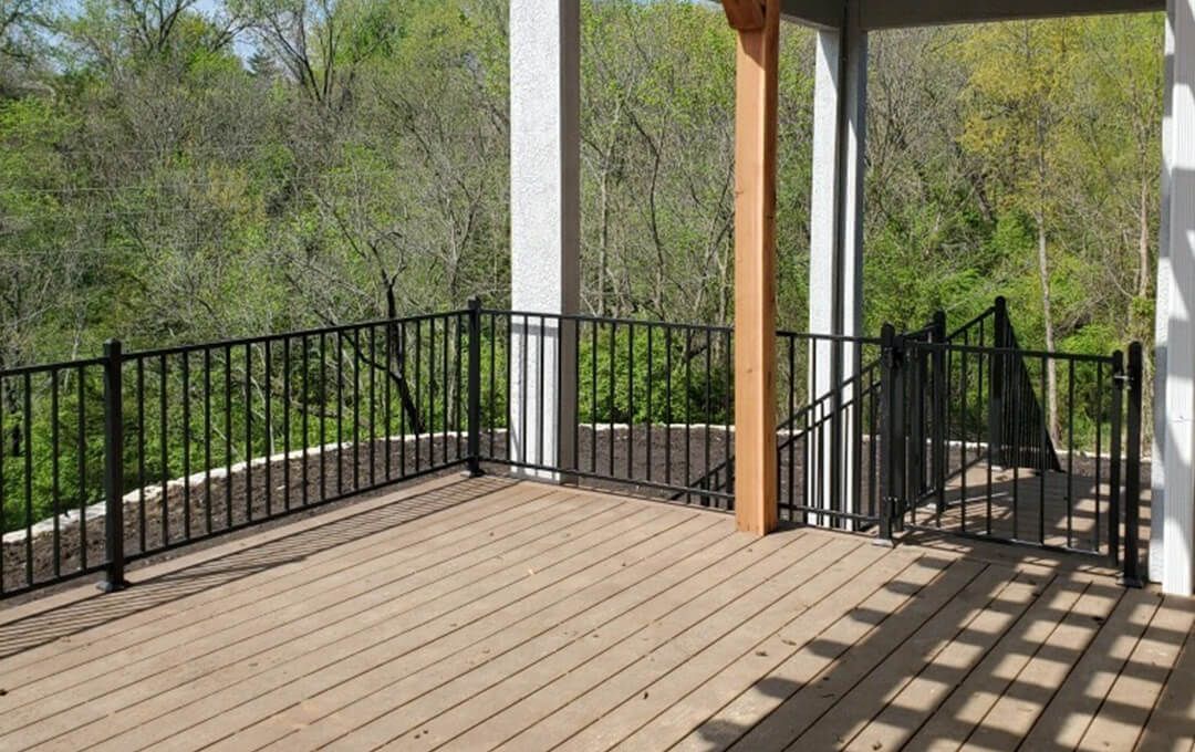 An empty deck with a metal railing and trees in the background.