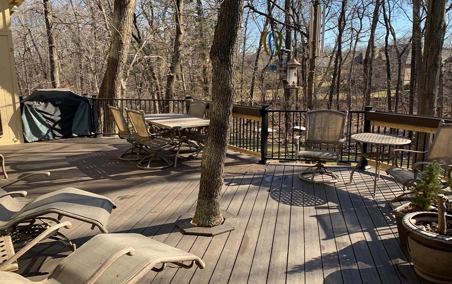 A large wooden deck with a table and chairs in the middle of the woods.