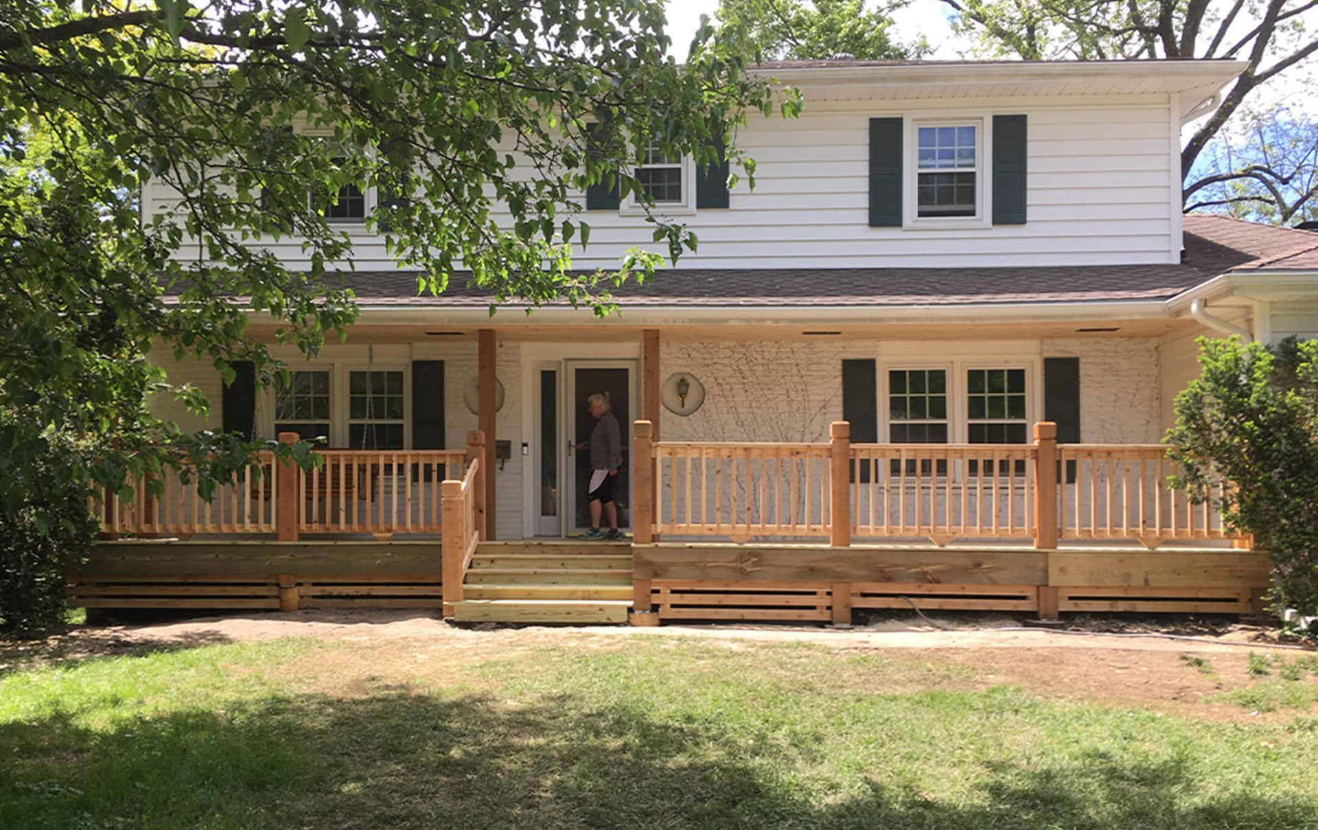 A man is standing on the front porch of a house with a wooden deck.