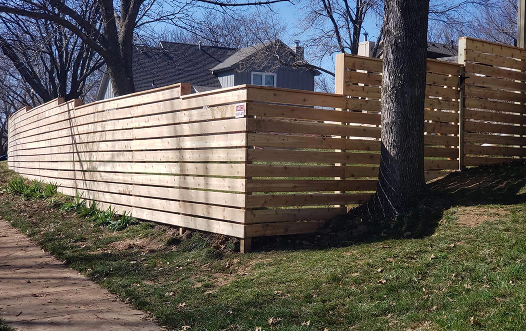 A wooden fence along a sidewalk with a house in the background