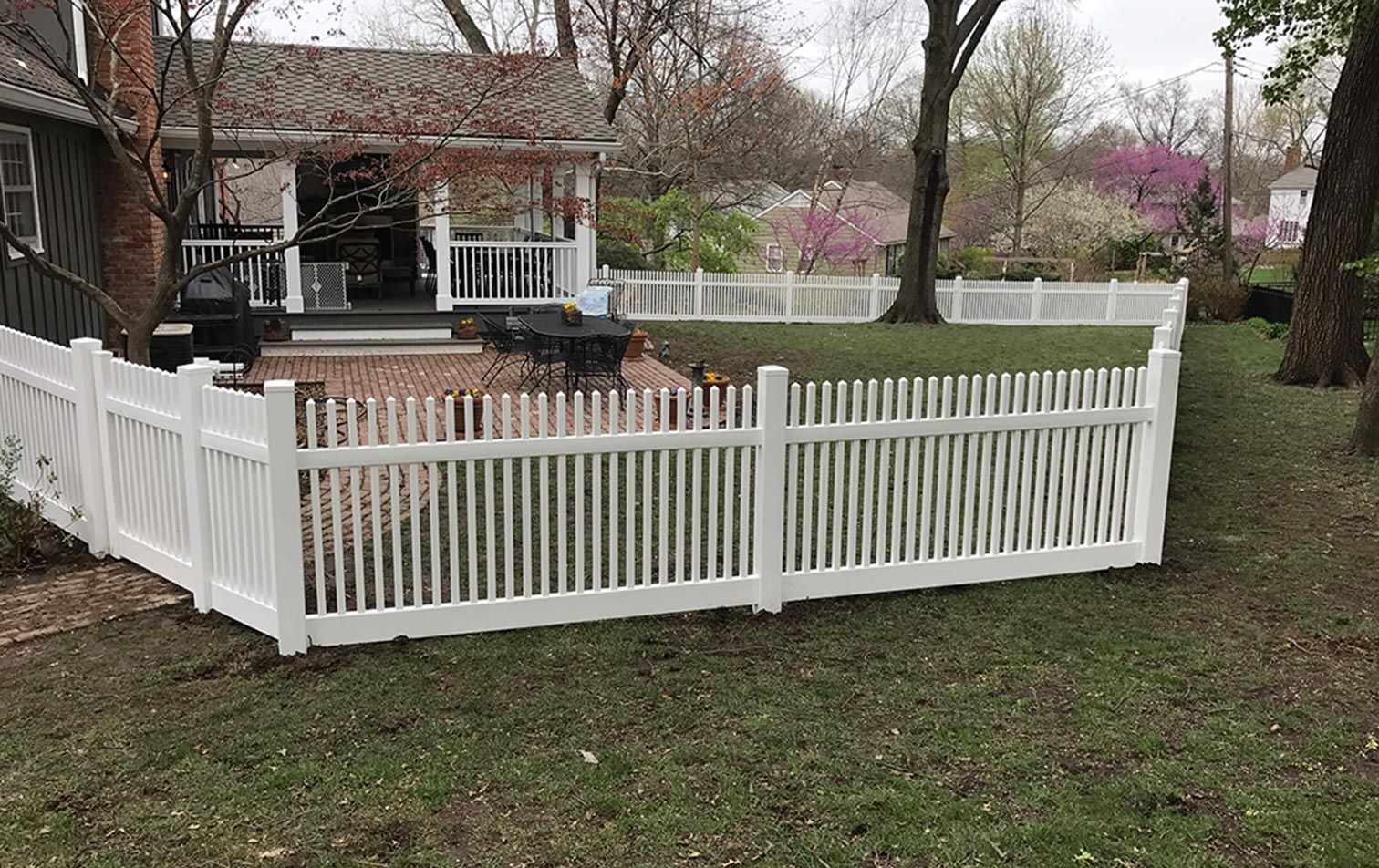 A white picket fence surrounds a backyard of a house.