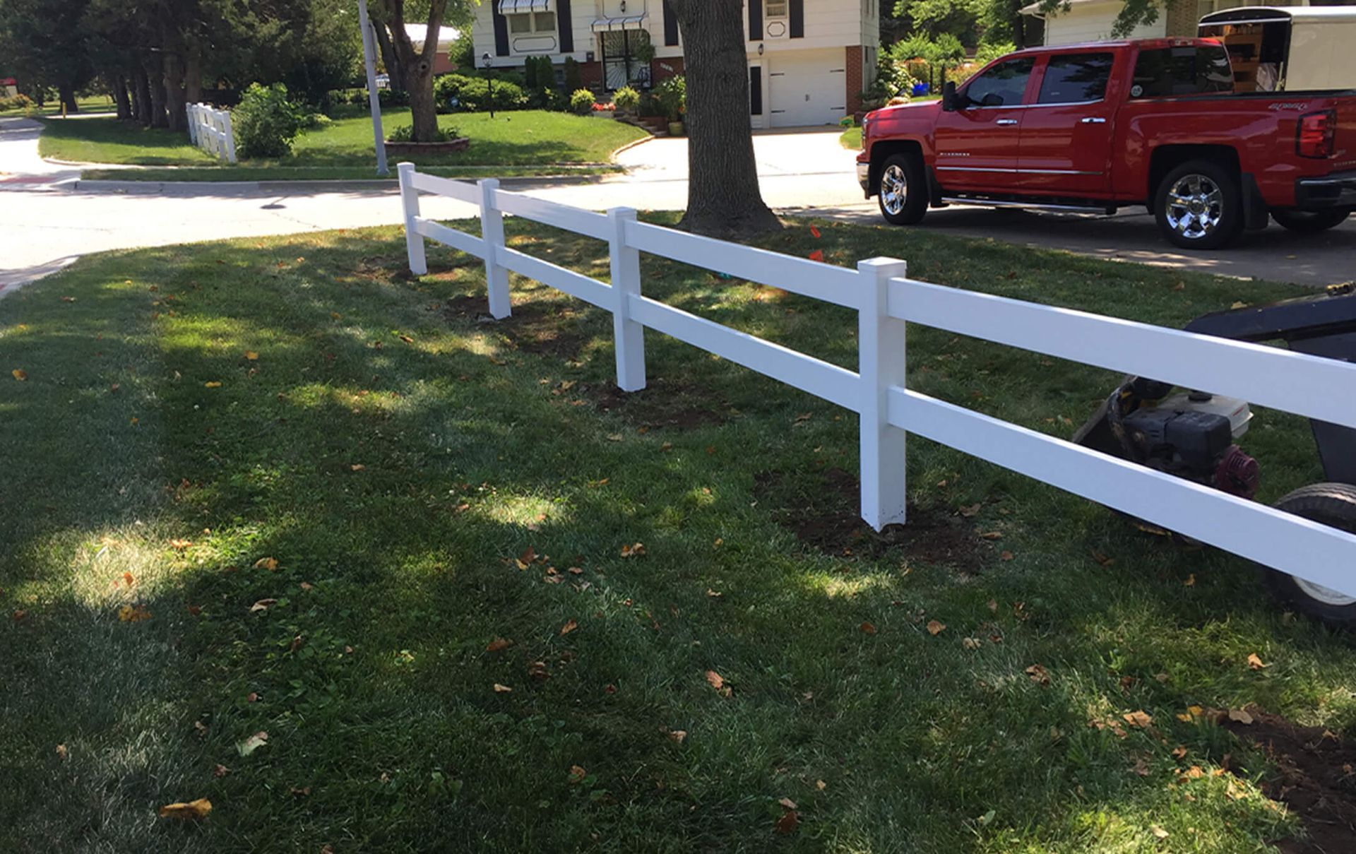 A red truck is parked in front of a white fence.