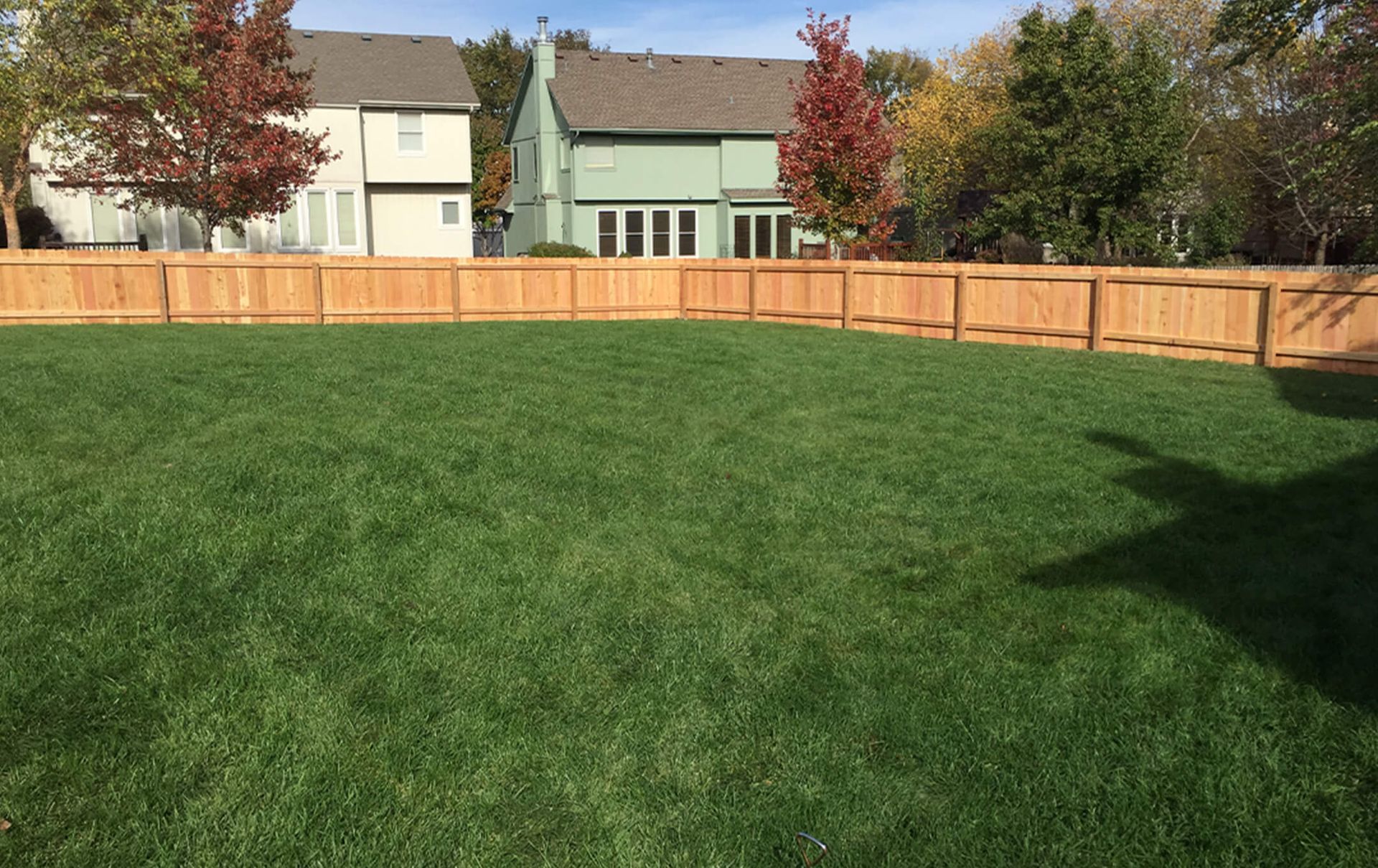 A large lawn with a wooden fence and a house in the background.