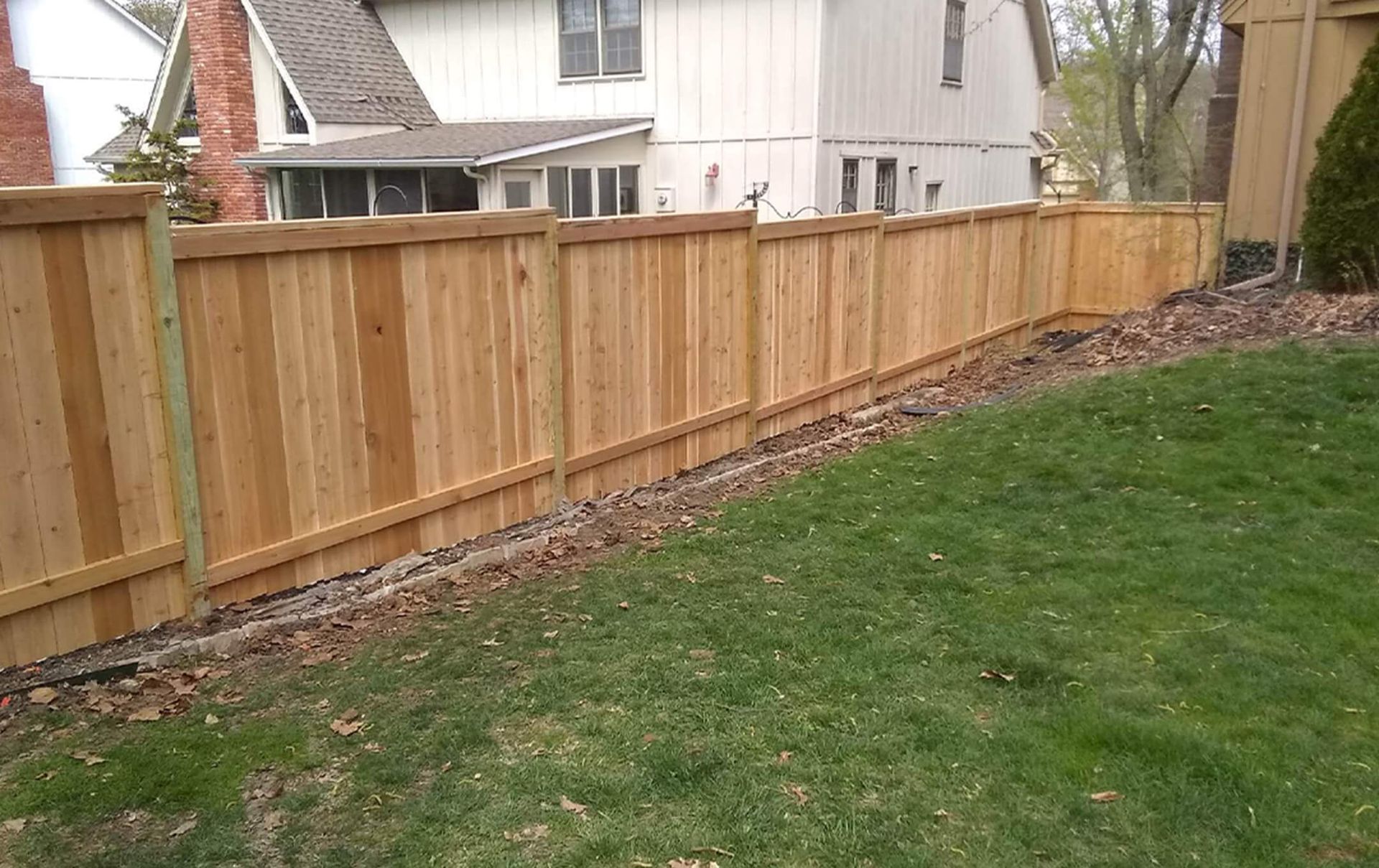 A wooden fence is in the backyard of a house.