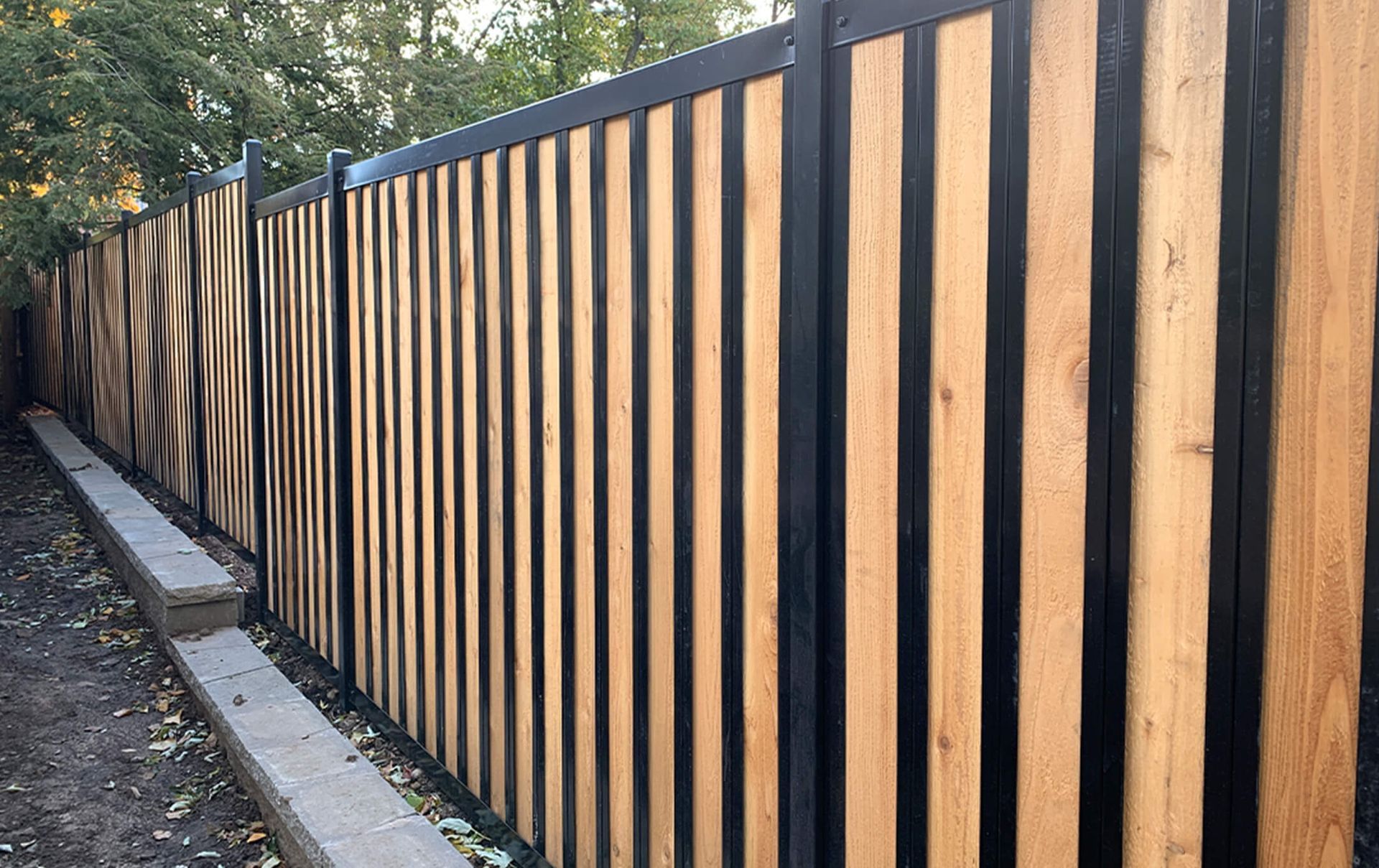 A wooden fence with a black metal frame is surrounded by trees.