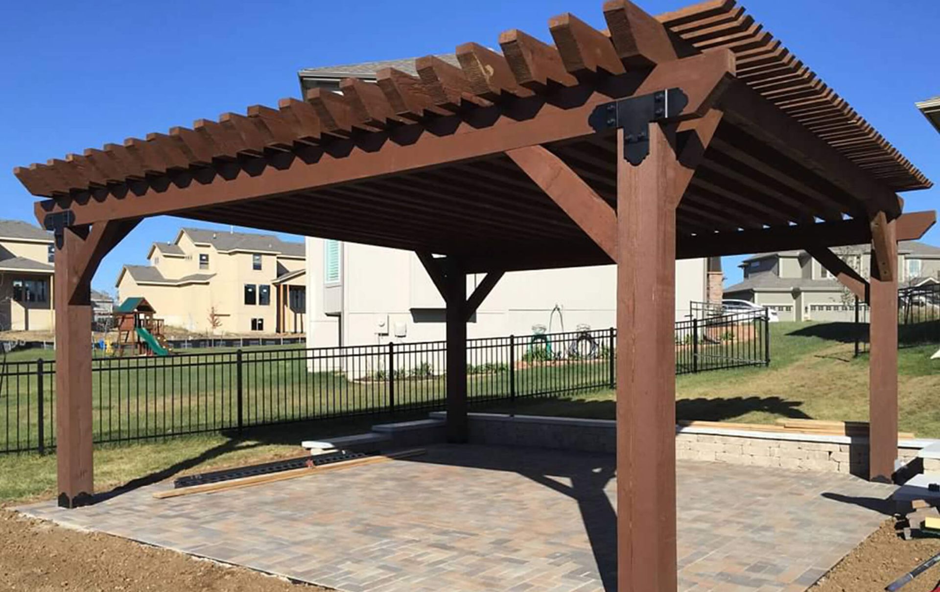A wooden pergola is sitting in the middle of a yard.