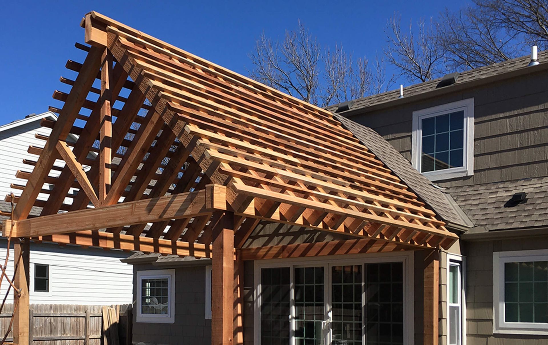 A wooden pergola is being built on the side of a house.