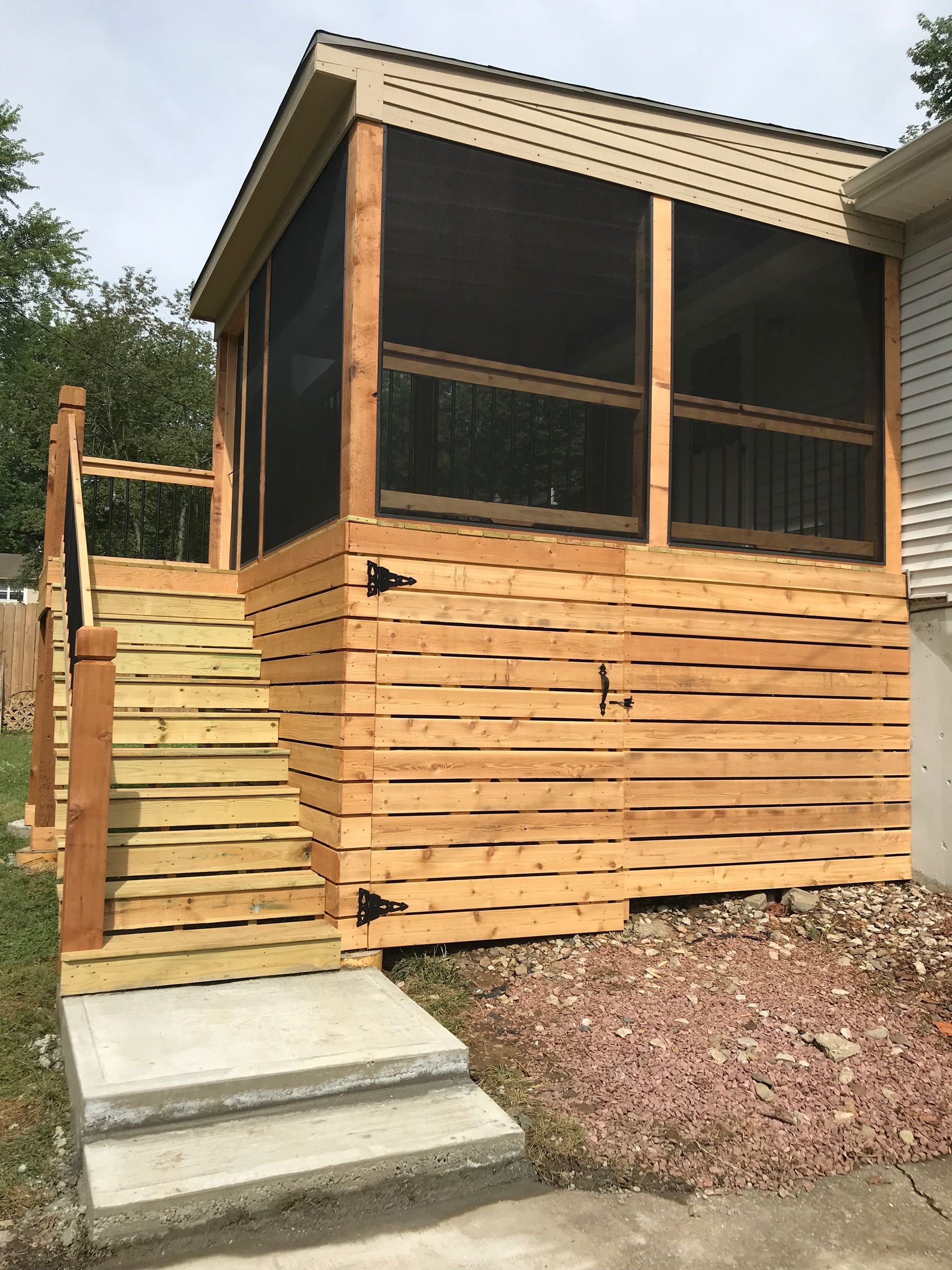 Screened-in porch addition with wood stairs and horizontal wood siding. Brown trim, black screening, and concrete steps.