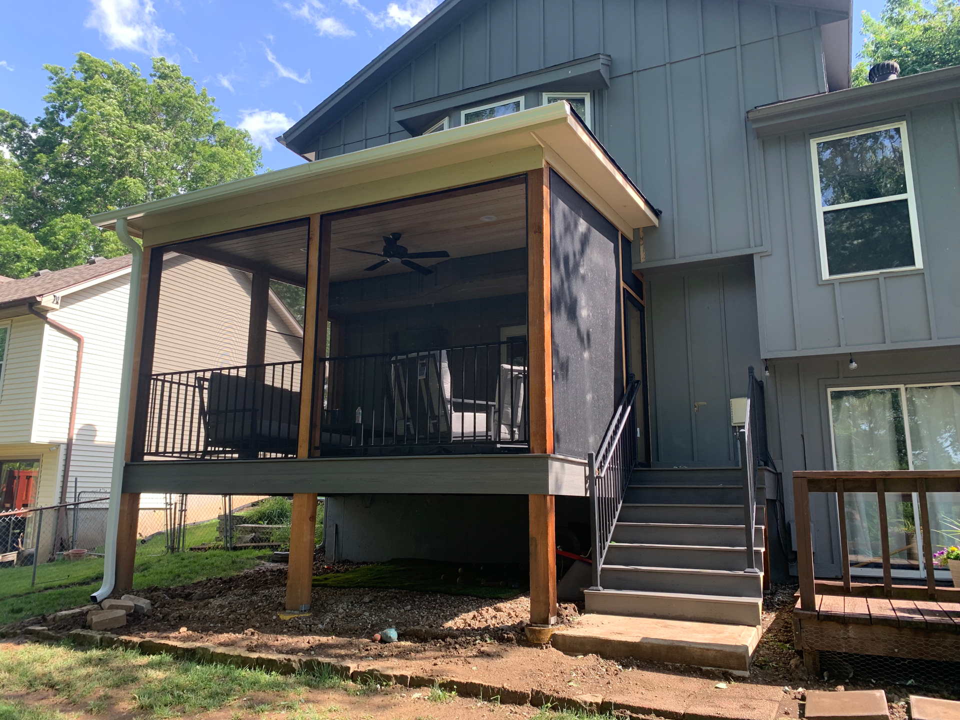 Screened-in porch attached to a gray house, with deck, steps, and black railing.