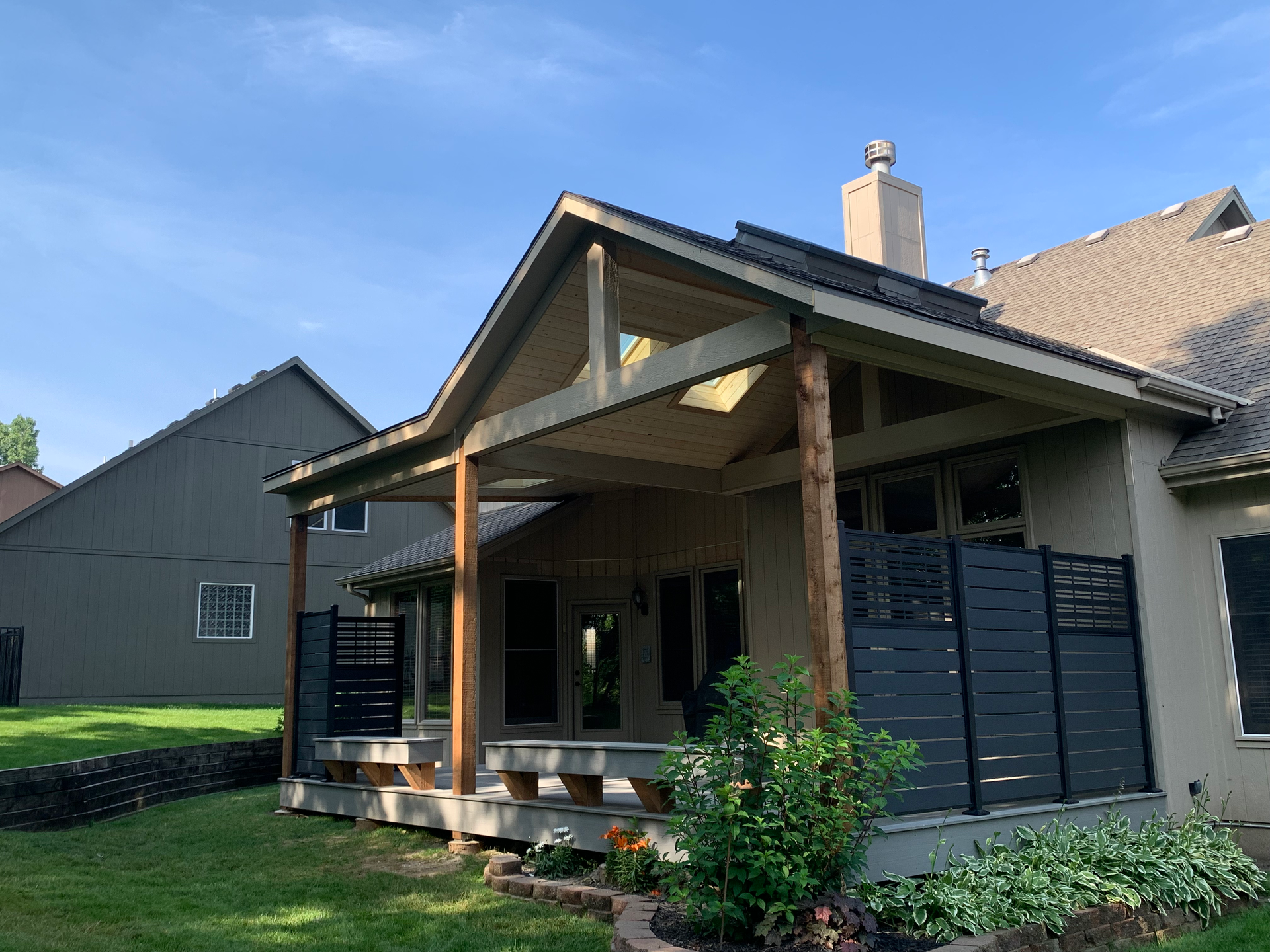 Covered patio with wood beams, dark gray fence, and green yard.