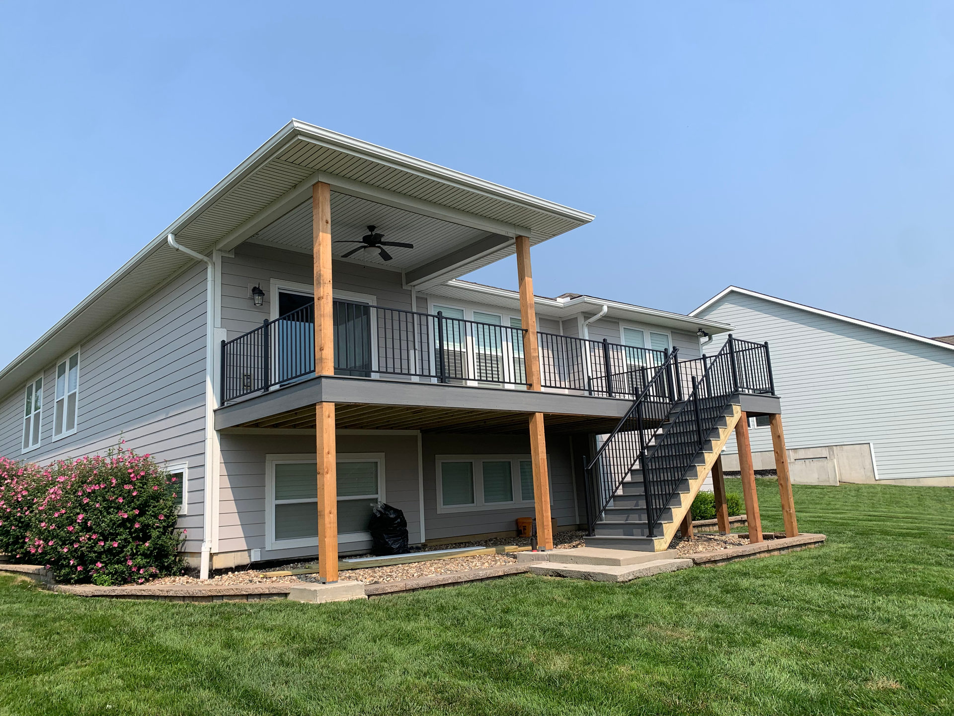 House with a covered deck, stairs, and gray siding; green lawn.