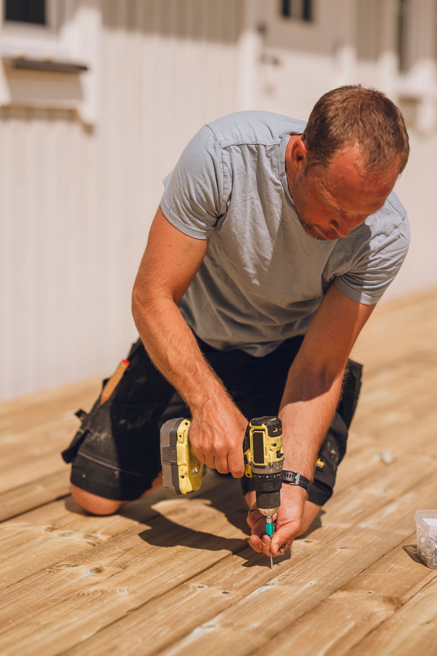 A man drills into lumber, showcasing skill and focus as a residential deck builder at work.