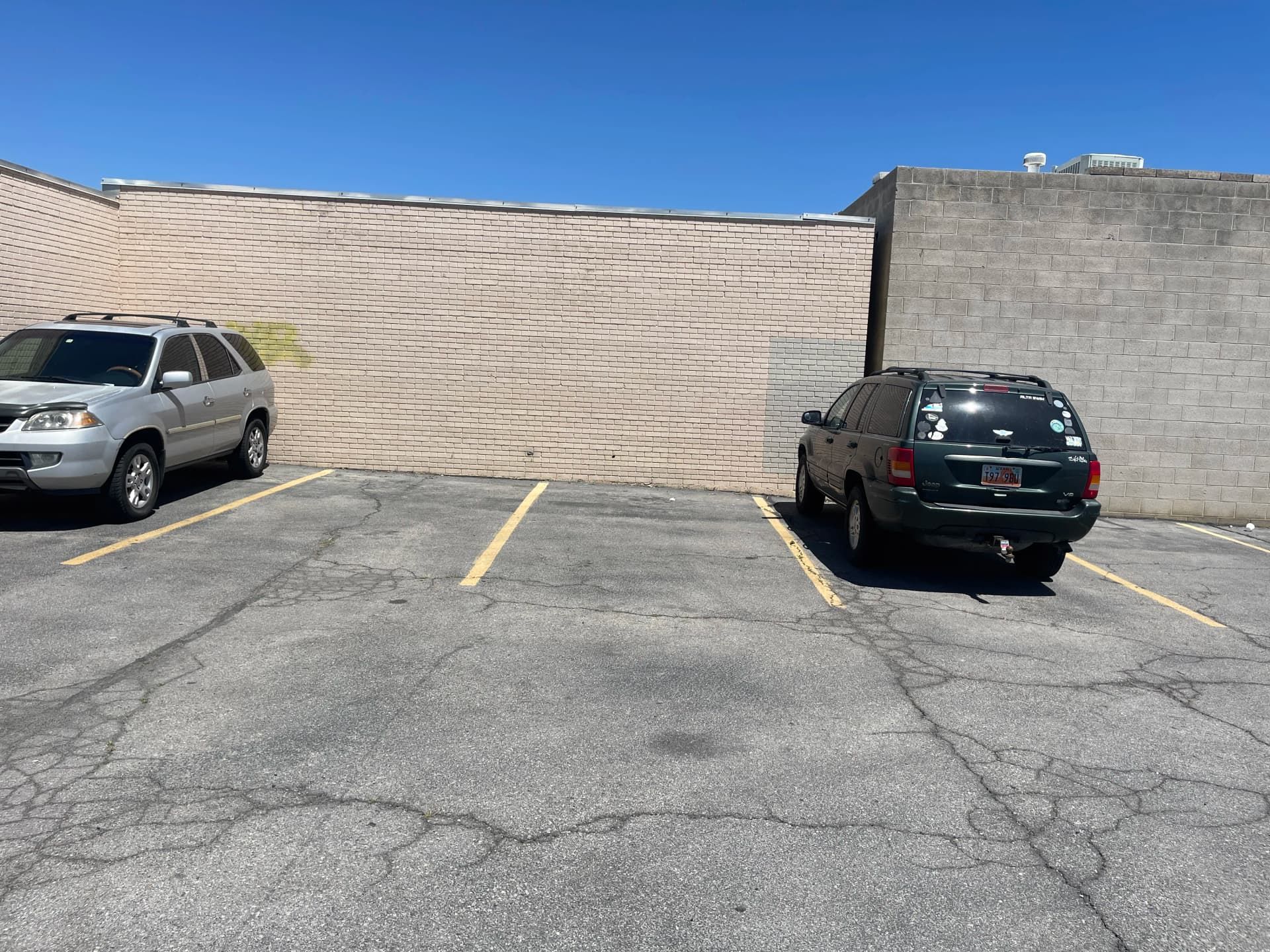 Parking lot with two parked SUVs beside a tan and gray brick wall under a clear blue sky.