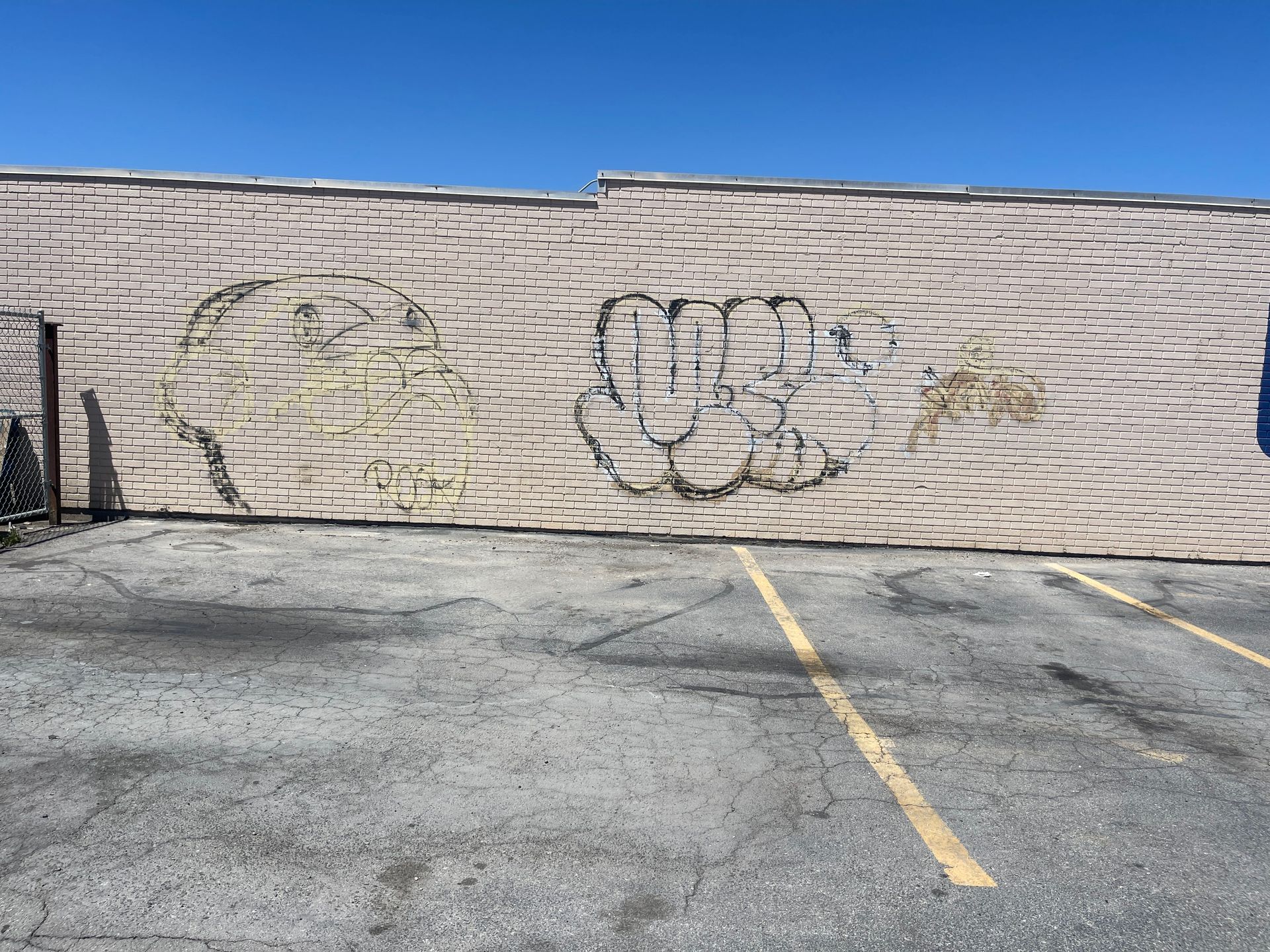 Graffiti on a tan brick wall beside an empty parking lot under a blue sky