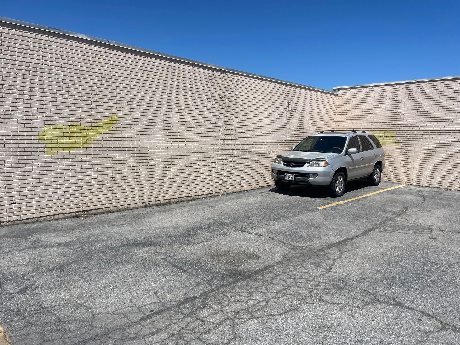 Silver SUV parked beside a large beige retaining wall in a cracked asphalt lot.
