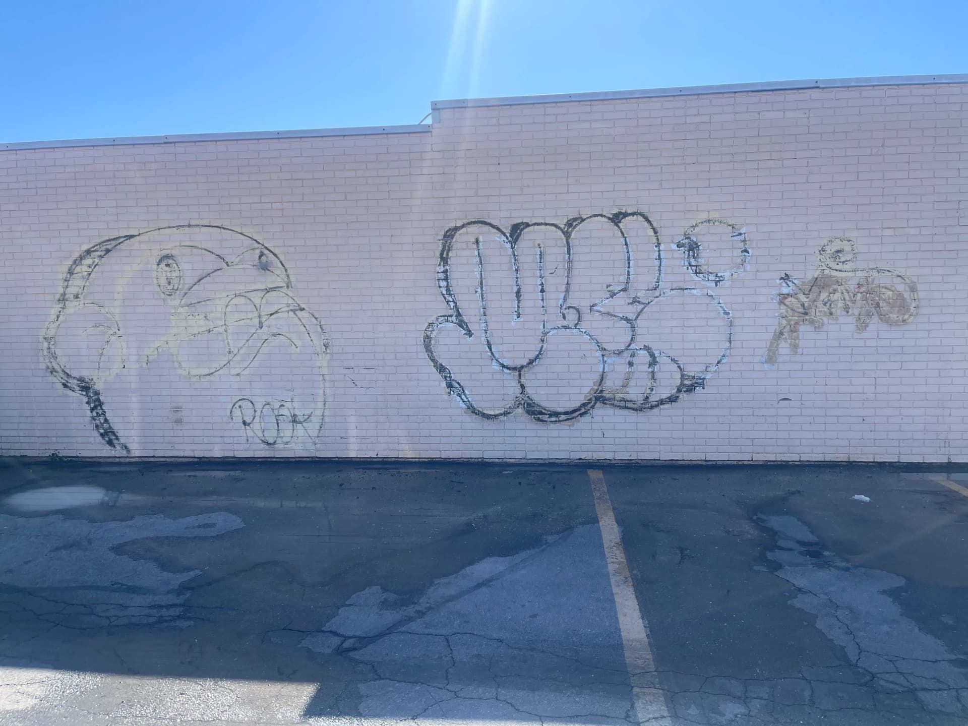 Graffiti on a white brick wall above an empty parking lot, including a face outline and bubble letters