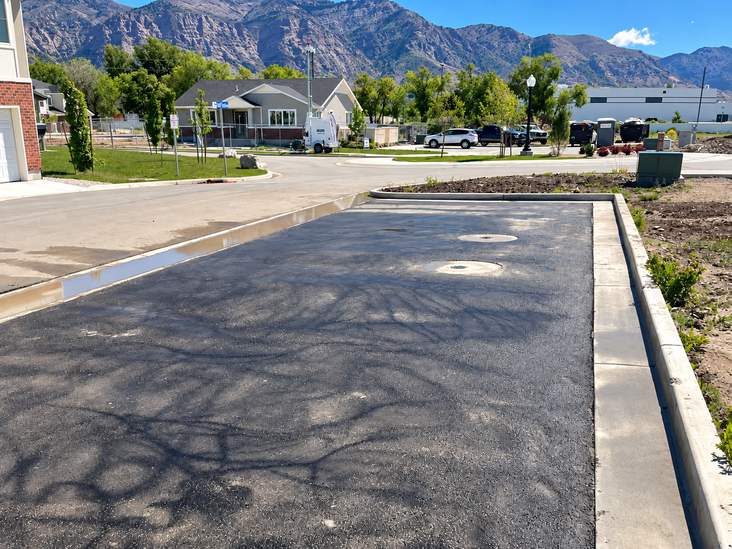 Freshly paved parking lane beside homes with mountains in the background