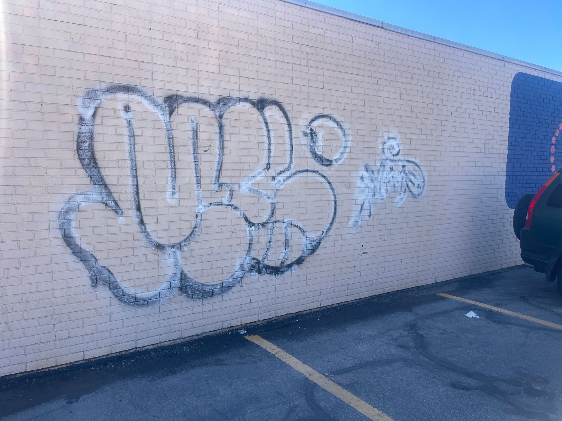 Graffiti on a beige brick wall in a parking lot beside a dark doorway.