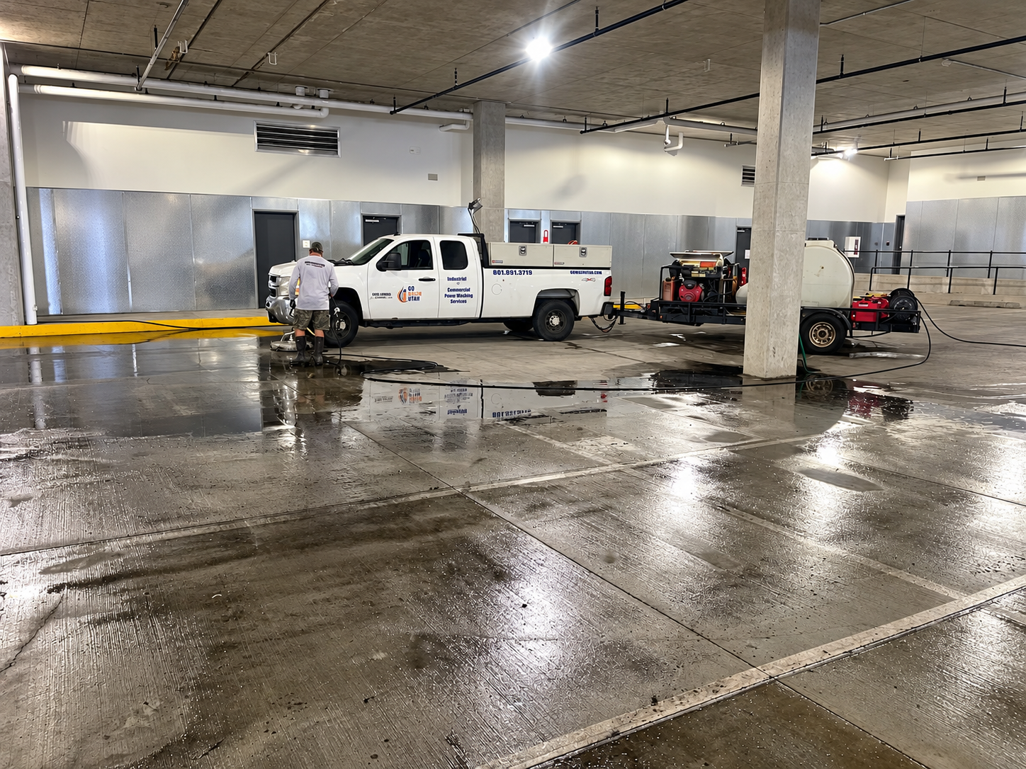 White pickup truck in a wet indoor garage, with a person working near the rear and another vehicle nearby