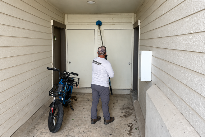 Person using a long-handled tool to reach a ceiling in a covered entryway beside a parked motorcycle.