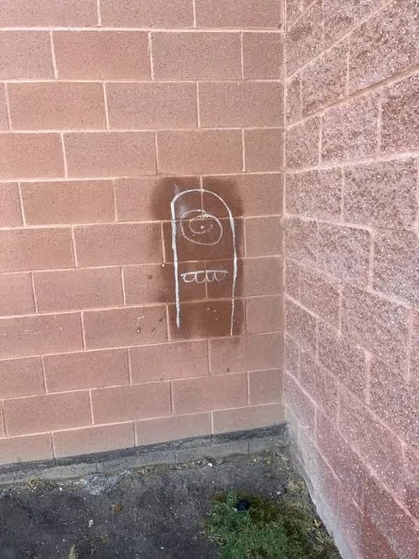 Small wall-mounted utility box on a tan brick corner wall with white graffiti and a concrete floor.