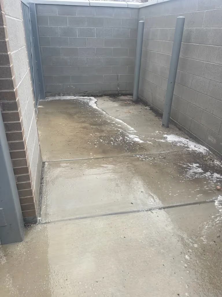 Narrow concrete courtyard with cinderblock walls and a wet, stained floor