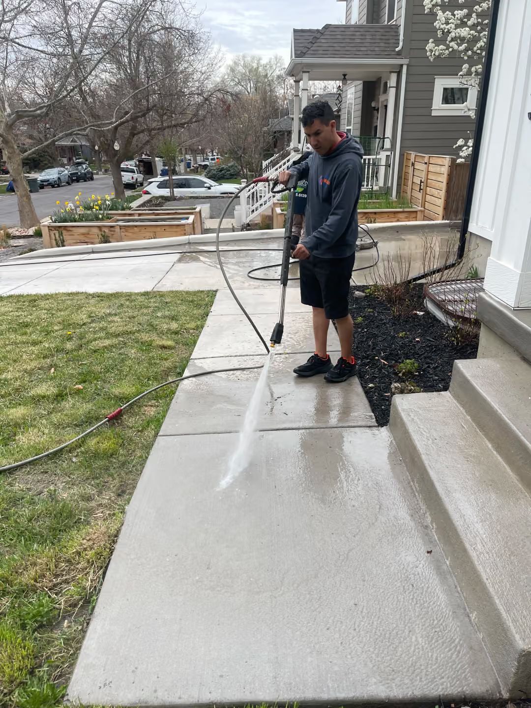 Person pressure-washing a concrete walkway beside a house and lawn.