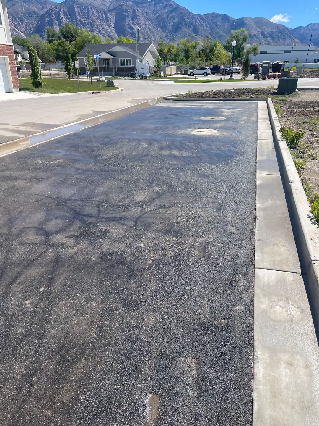Freshly paved asphalt road beside a curb in a quiet residential area with mountains in the background