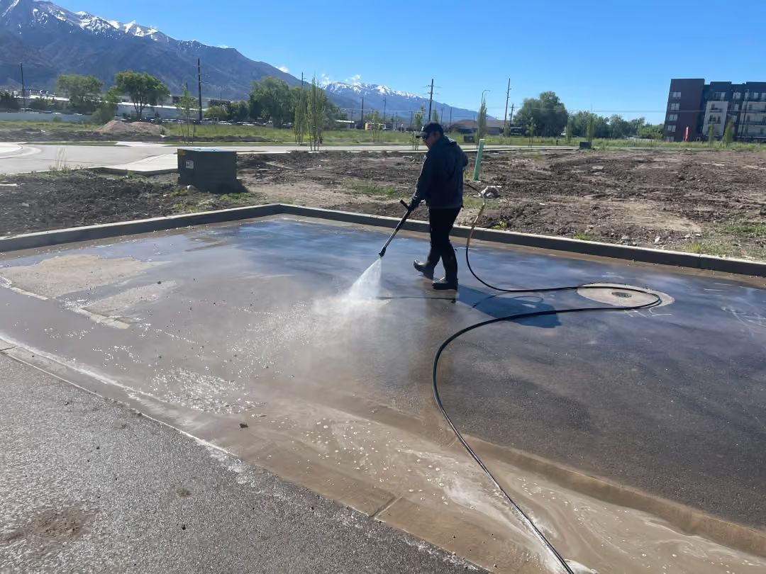 Person pressure-washing a wet concrete slab outdoors with mountains in the background