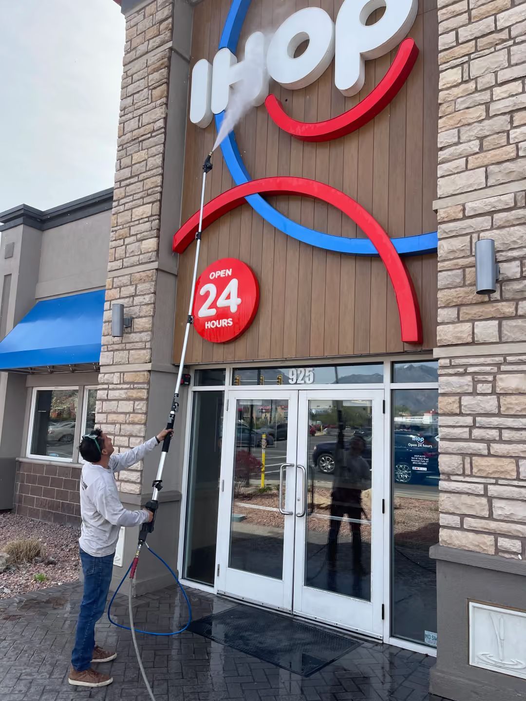 Person cleaning the IHOP sign above the restaurant entrance with a long pole