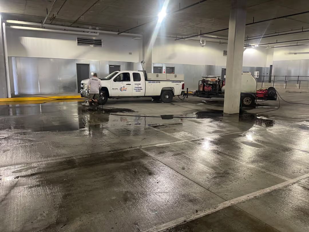 White pickup truck and a small utility cart in a wet indoor parking garage under bright lights.