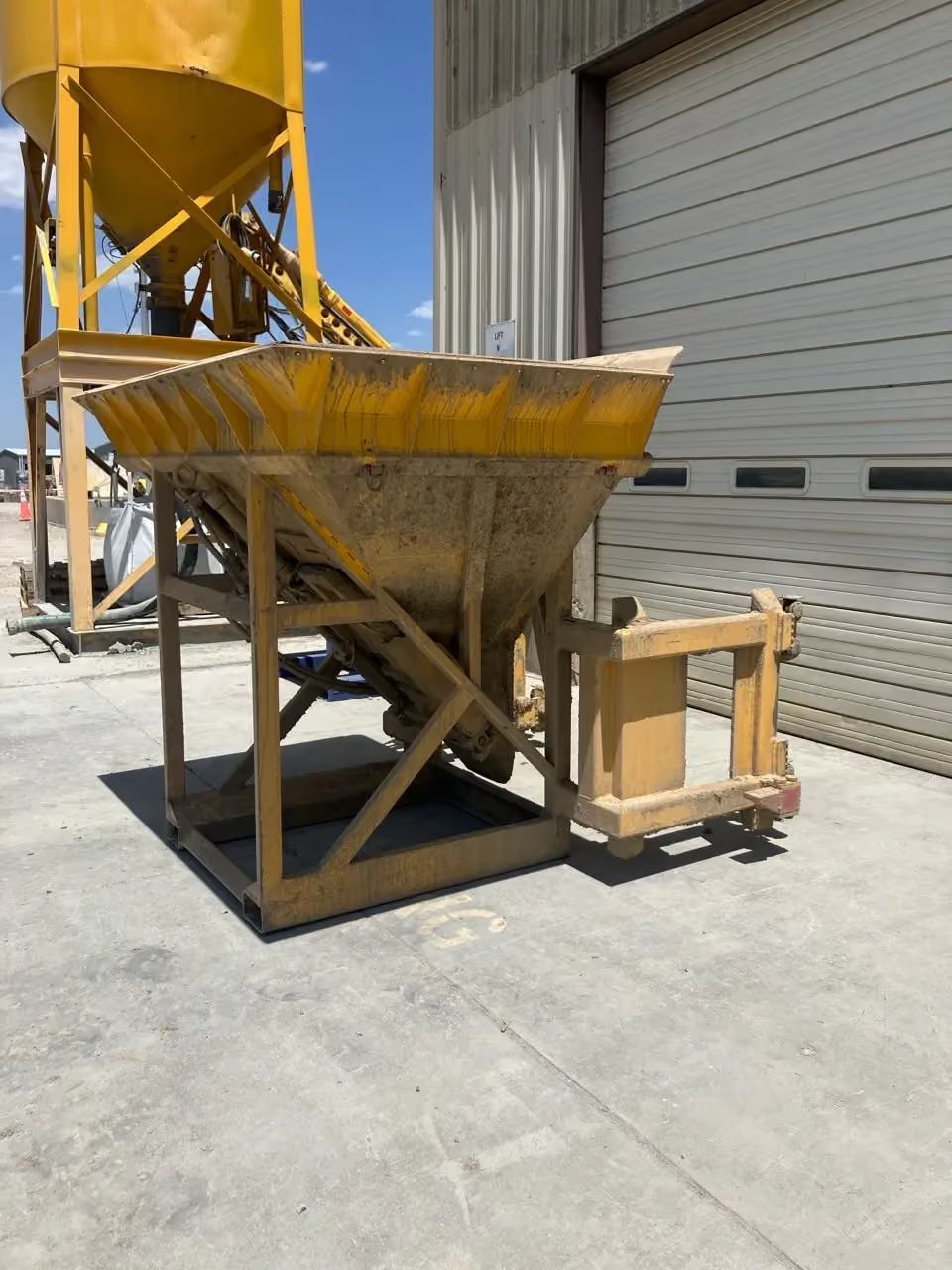 Industrial yellow hopper next to a warehouse wall on a concrete lot