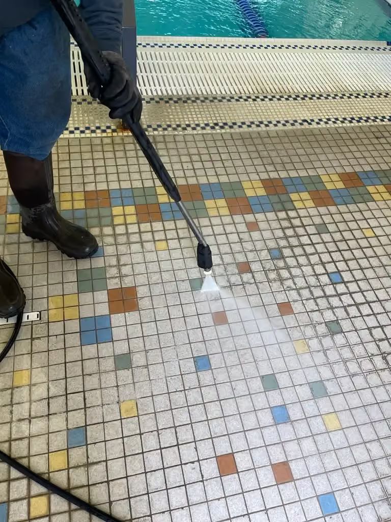 Person pressure-washing a multicolored tiled sidewalk with a spray wand