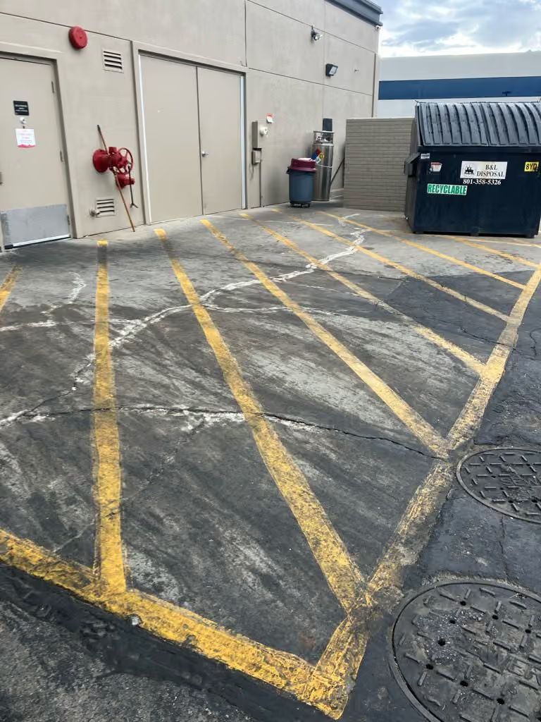 Marked industrial loading area beside a building, with yellow crosshatched pavement and a dumpster.