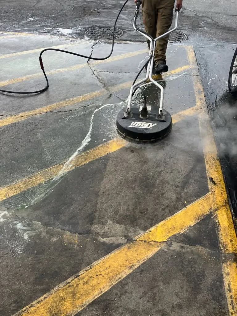 Person pressure-washing a parking lot with yellow painted lines, water spraying across the pavement.