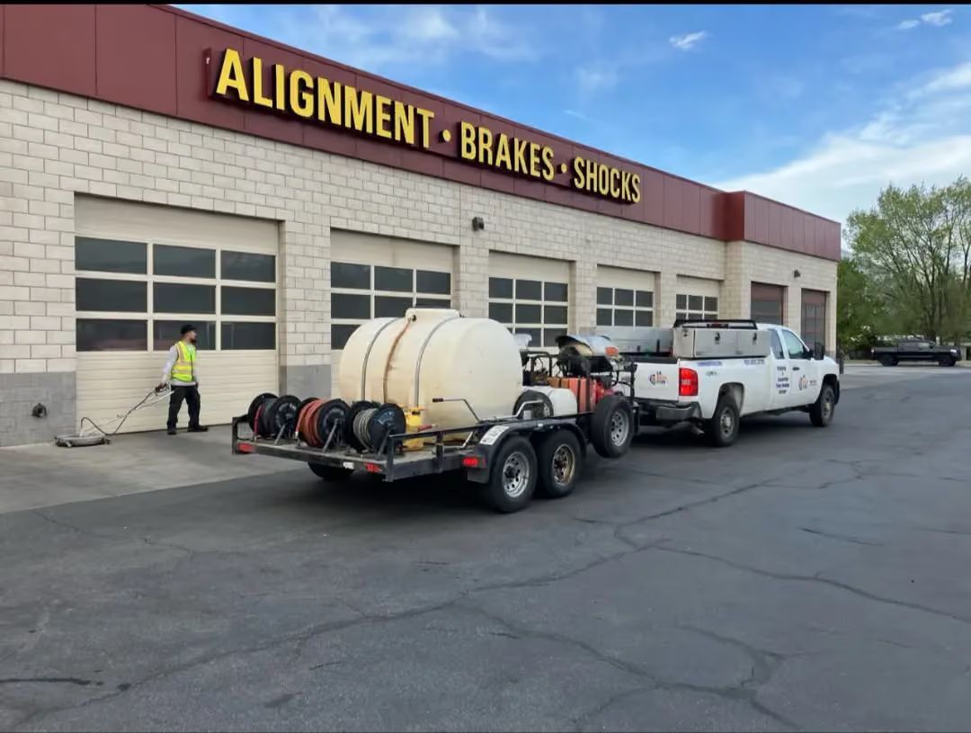 White pickup towing a trailer with a tank outside an auto shop labeled “Alignment Brakes”