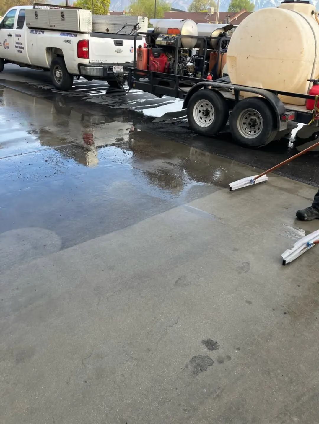 White pickup truck and trailer with equipment beside a wet concrete lot and puddles