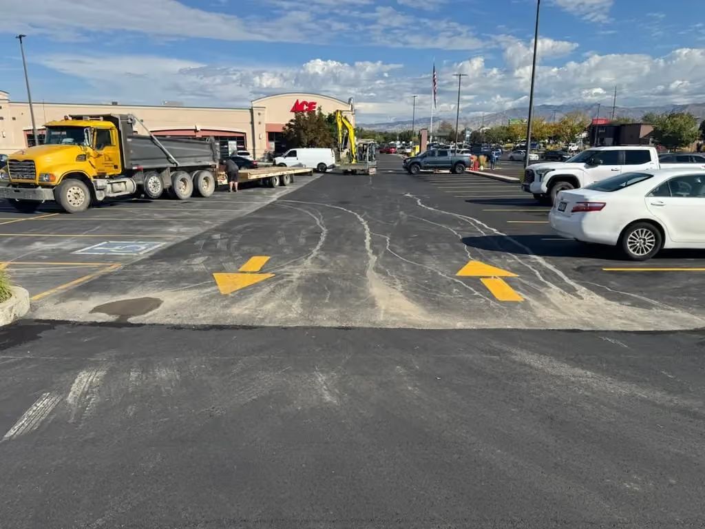 Parking lot with yellow arrows, trucks on the left, and white cars on the right under a cloudy sky