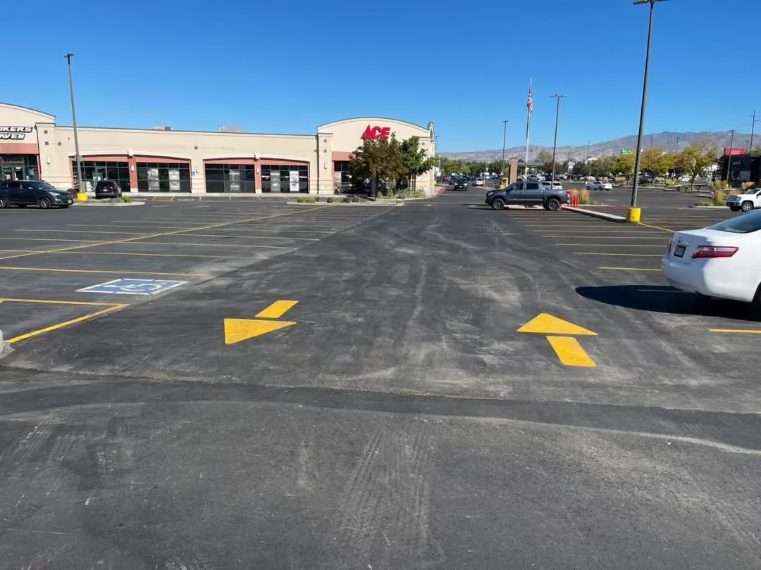 Parking lot with yellow directional arrows, storefronts, and a few parked cars under a clear sky