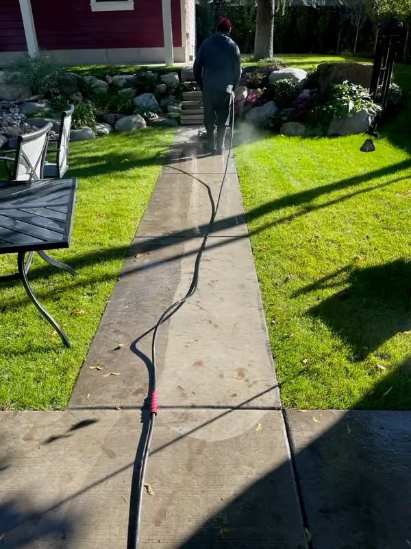 Person walking on a garden path with a long black cable across the sidewalk.