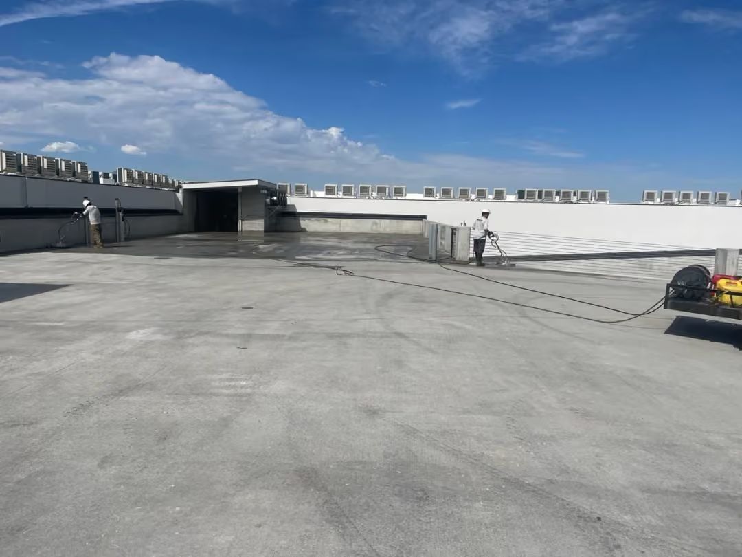 Wide concrete rooftop with vents and a person standing near the center under a blue sky.