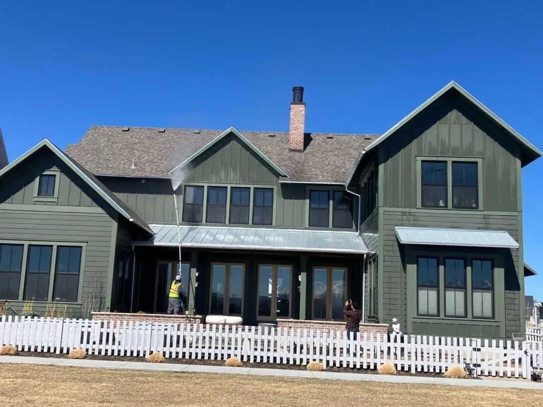 Large green house with white picket fence and porch under a clear blue sky