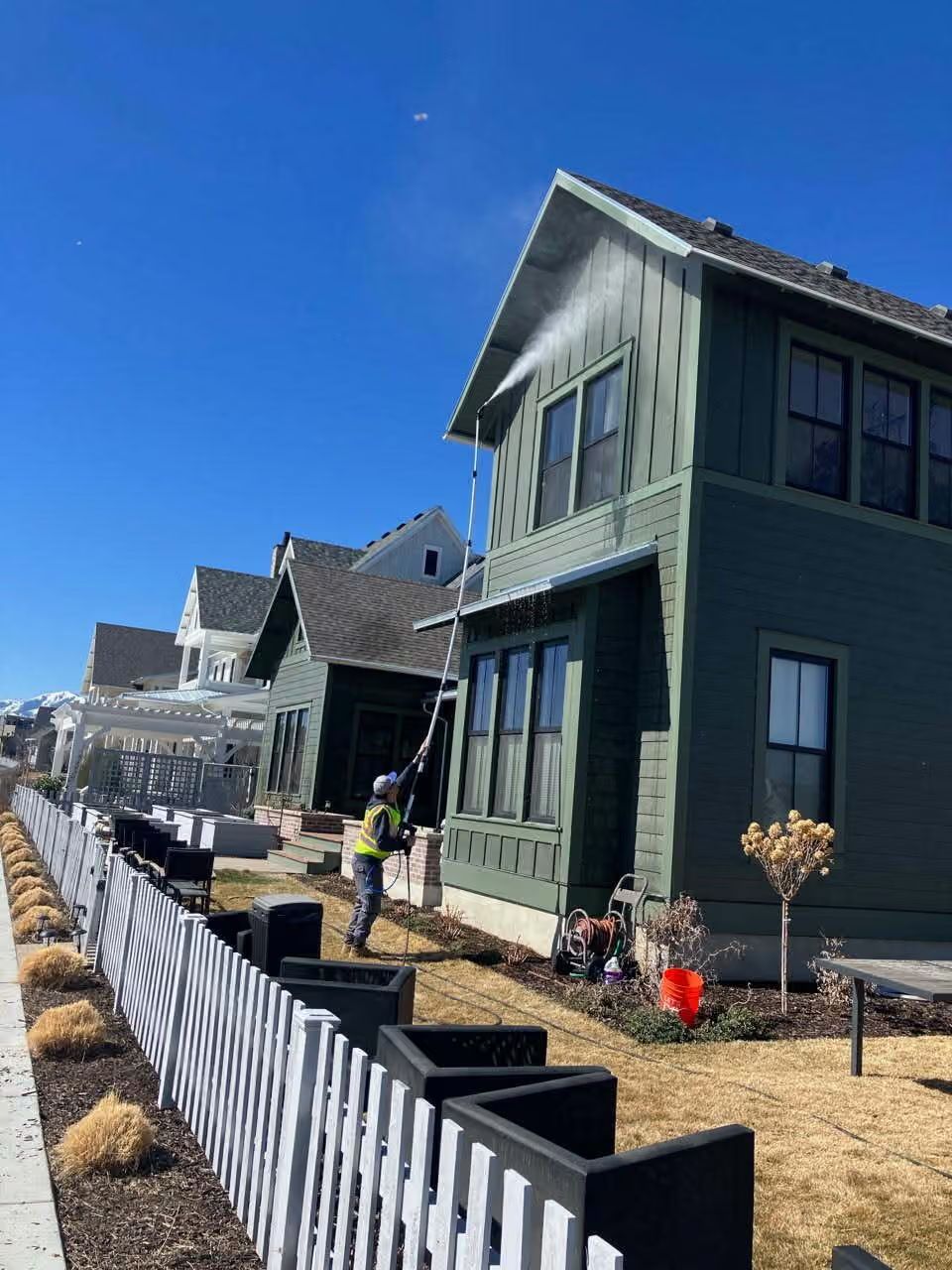 Row of new houses under construction beside a black-and-white fence on a sunny day