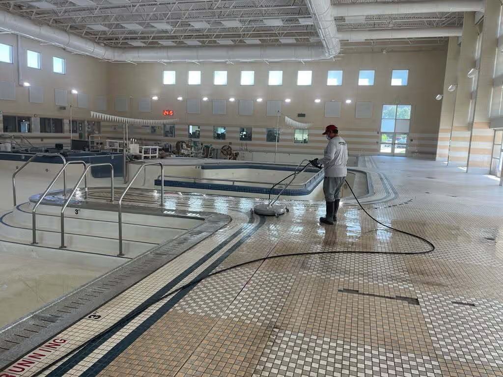 Indoor swimming pool under construction, with a worker standing beside the empty pool basin.
