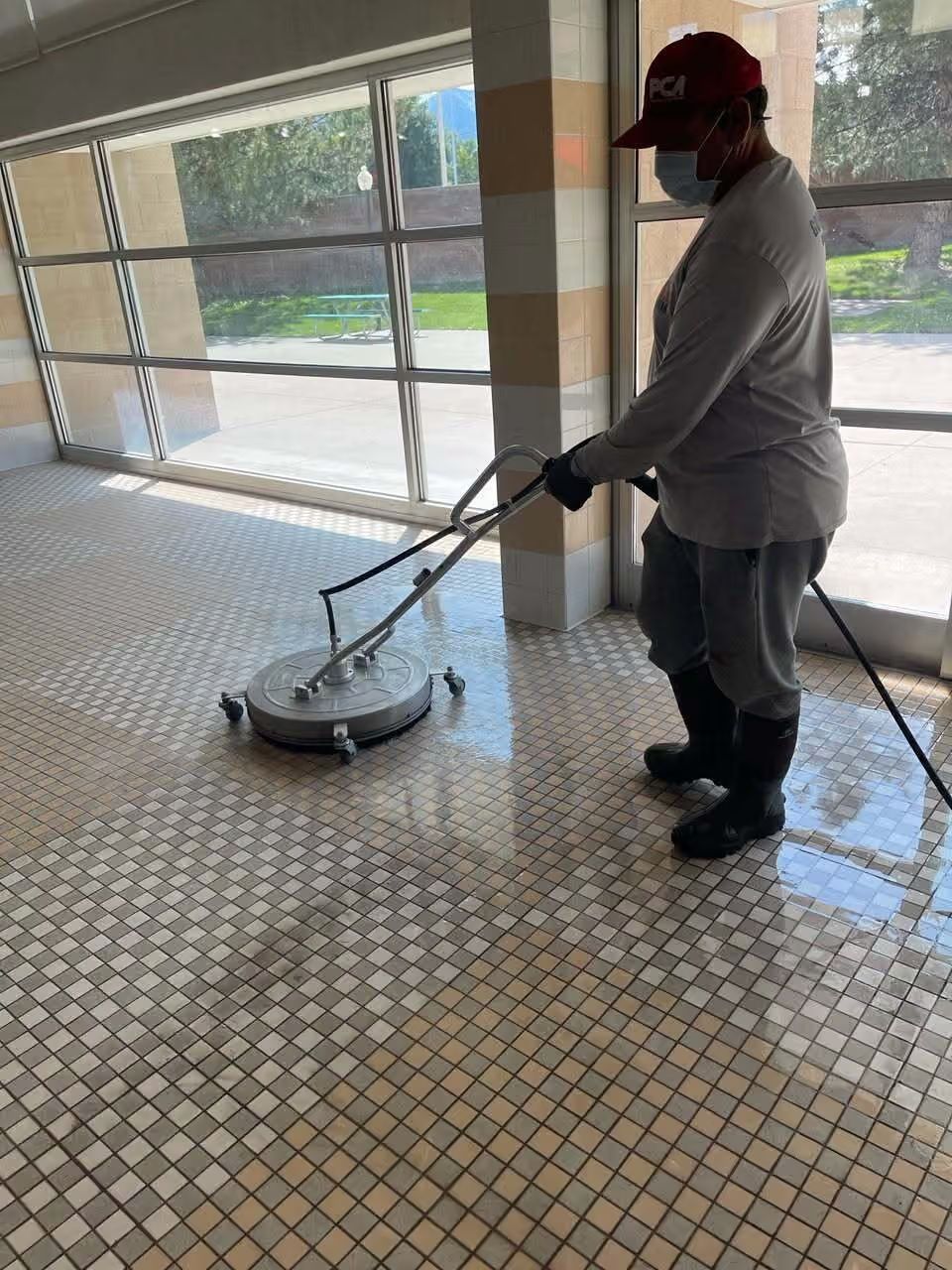 Worker cleaning a tiled floor with a floor buffer in a bright indoor lobby